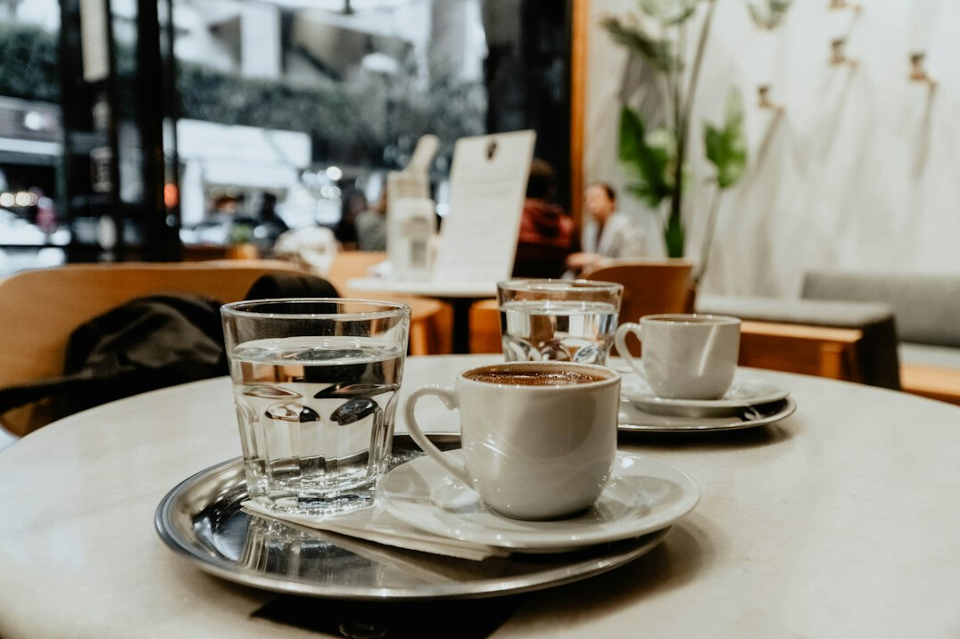 Two cups of coffee on a small round table in a bright cafe